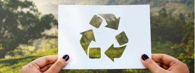 Foto de uma mão segurando um papel com o simbolo de reciclagem